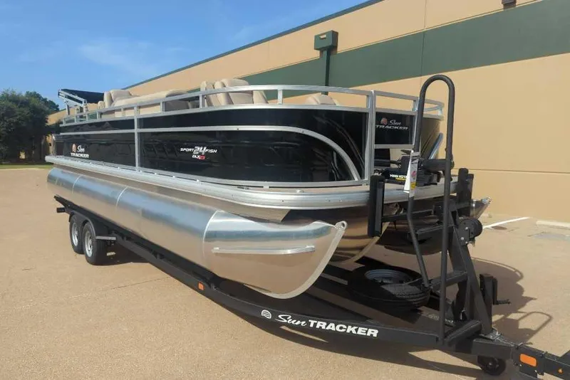 Slide: The Image of 2025 Sun Tracker Sportfish 24 XP3 pontoon boat on trailer, parked outdoors. - 16