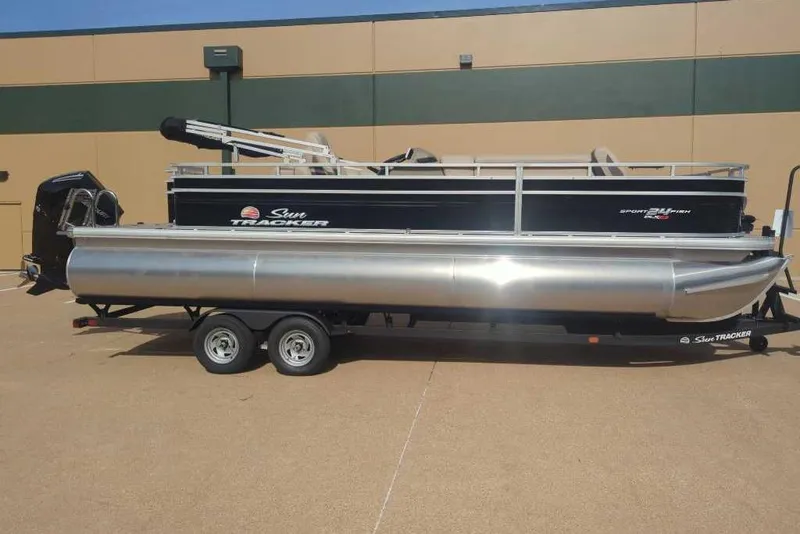 Slide: The Image of 2025 Sun Tracker Sportfish 24 XP3 pontoon boat on trailer, parked outdoors. - 2