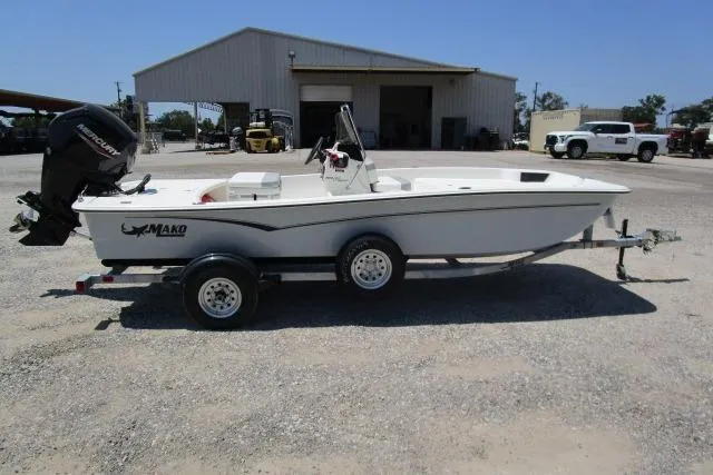 Slide: The Image of 2023 Mako Pro Skiff 17 CC boat on trailer, parked outdoors near a warehouse. - 2