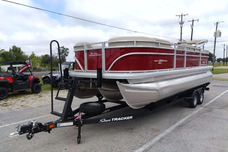 Slide: The Image of 2025 Sun Tracker Party Barge 22 RF XP3 pontoon boat on trailer, parked outdoors. - 2