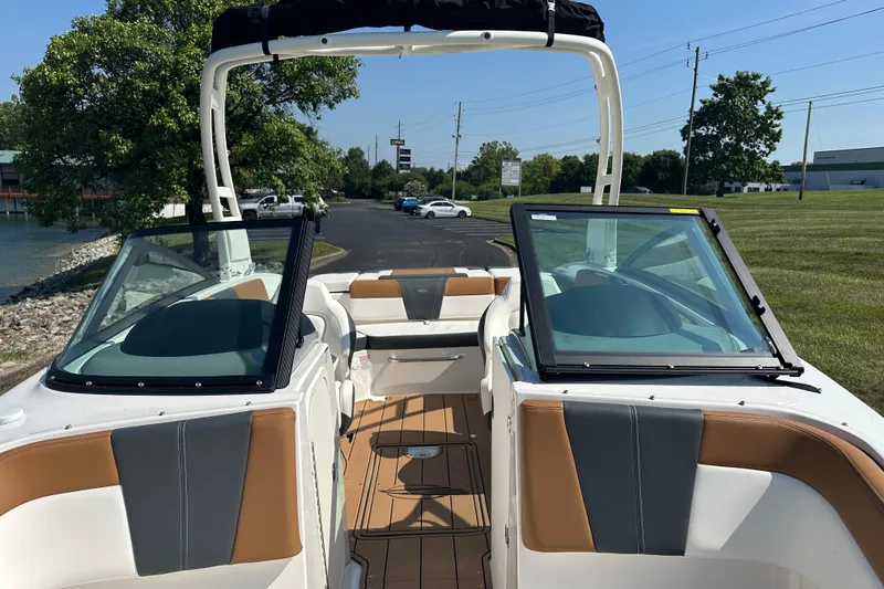 Slide: The Image of 2026 CHAPPARRAL 23 SSi boat interior with tan and gray seating, docked near a grassy area. - 17