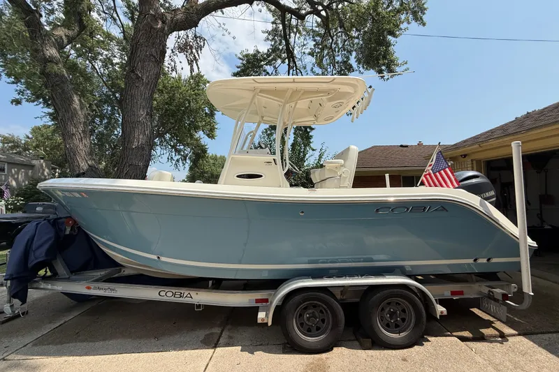 Slide: The Image of 2020 Cobia 220 Center Console boat on trailer, parked in driveway with American flag. - 2