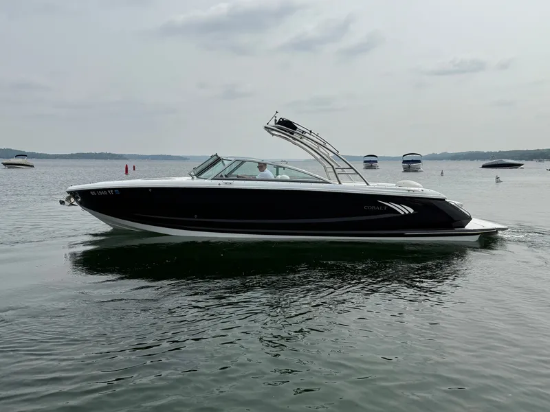 Slide: The Image of 2016 Cobalt A28 boat cruising on a calm lake with other boats in the background. - 1
