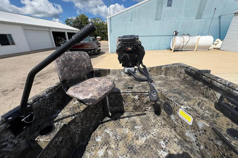 Slide: The Image of 2026 Excel Eclipse boat interior with camouflage seating and motor, parked outdoors. - 15