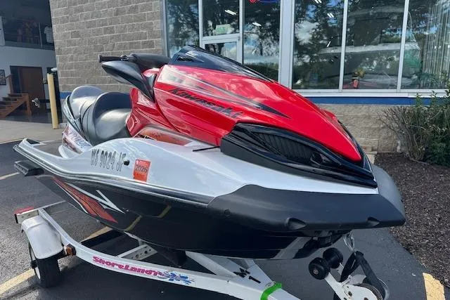 Slide: The Image of 2012 Kawasaki Ultra LX jet ski in red and white on a trailer, parked outdoors. - 6