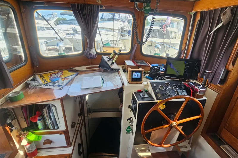 Slide: The Image of Cozy 1982 Nordic Tug 26 helm with wooden wheel, navigation equipment, and marina view. - 14