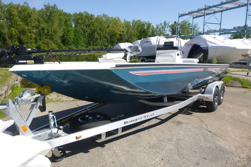 Slide: The Image of 2025 Ranger RB210 boat on trailer, parked outdoors near trees and other boats. - 2