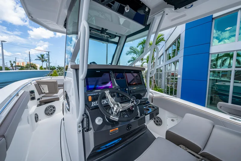 Slide: The Image of 2019 Blackfin 272 CC boat cockpit with modern controls and seating, docked near a blue building. - 16