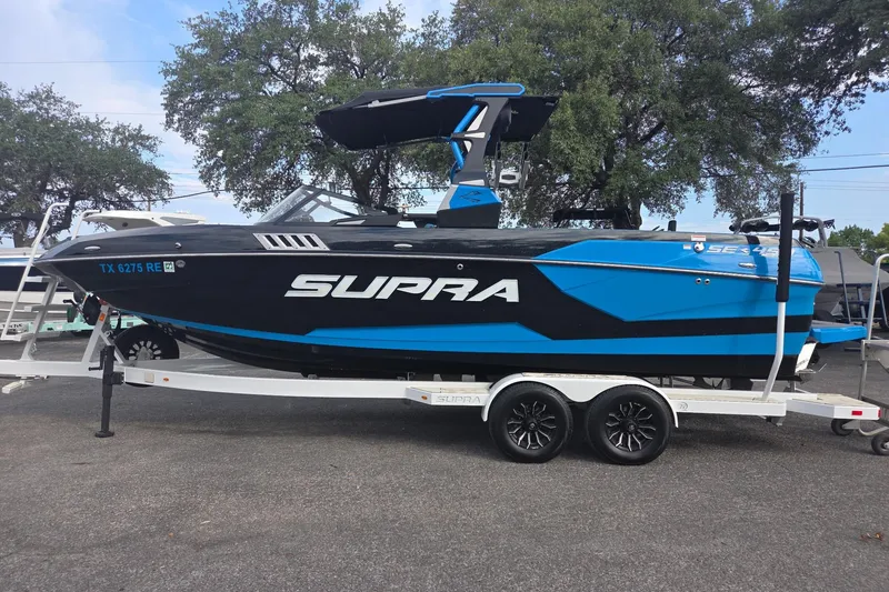 The Image of 2021 Supra SE 450 boat in blue and black on a trailer, parked outdoors. - 1