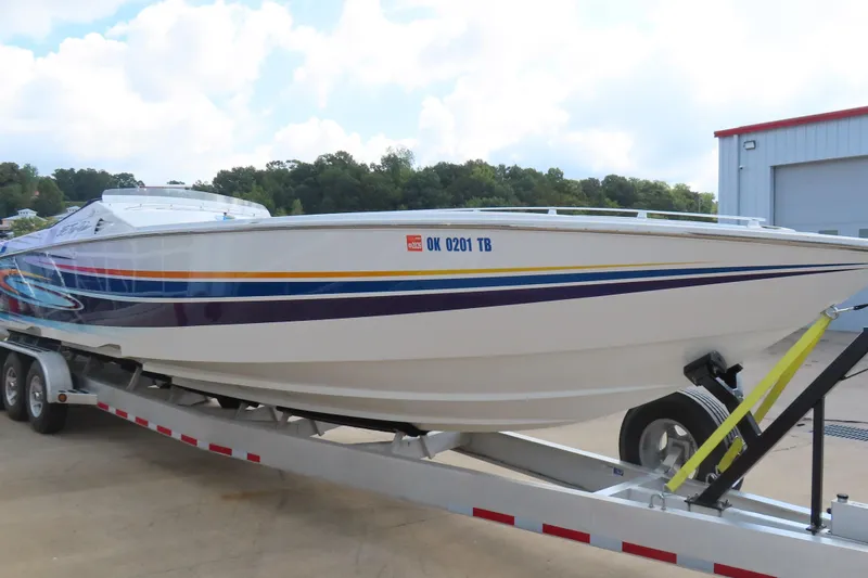 Slide: The Image of 2004 Cigarette 38 Top Gun TS boat on trailer, vibrant stripes, parked outdoors. - 11