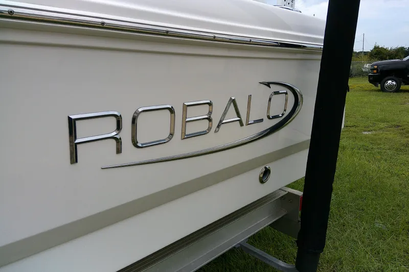 Slide: The Image of 2021 Robalo 246 Cayman boat logo on white hull, parked on grass. - 5