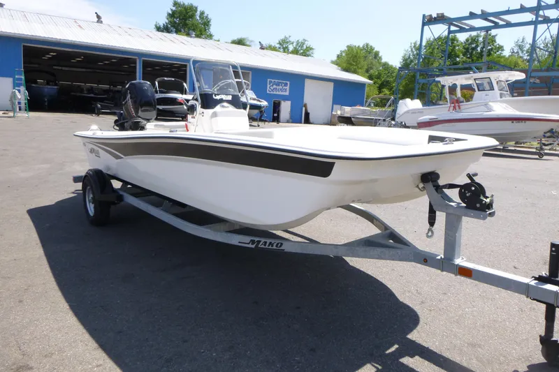 Slide: The Image of 2024 Mako Pro Skiff 17 CC boat on trailer, parked outdoors near a blue building. - 3