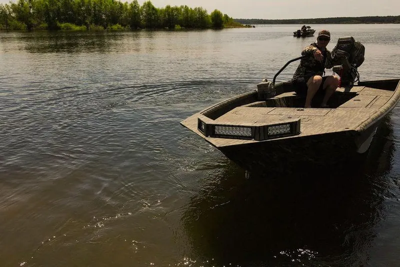 Slide: The Image of 2026 SeaArk 1752 Slayer X Pro boat on a calm lake with a person steering. - 11