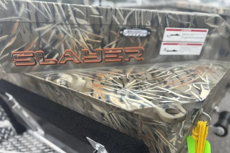 Slide: The Image of 2026 SeaArk 1752 Slayer X boat with camouflage design, parked near vehicles. - 16