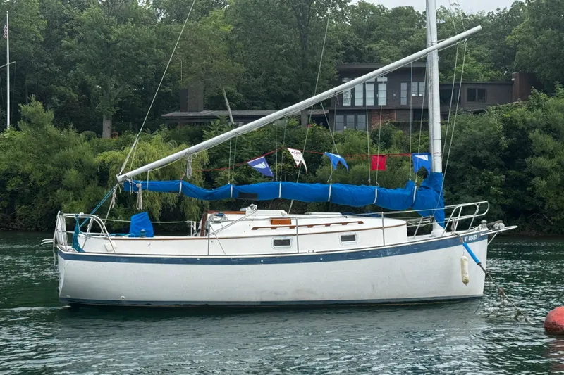 The Image of 1984 Nonsuch 26 Classic sailboat moored on a calm river, surrounded by lush greenery. - 0