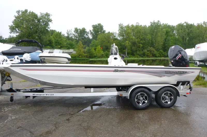 Slide: The Image of 2025 Ranger RB210 boat on trailer, parked near a lake with trees in the background. - 1