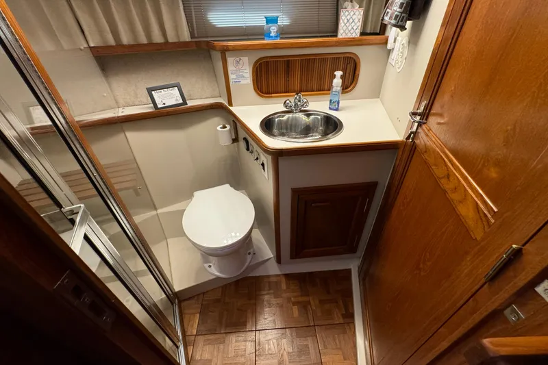 Slide: The Image of 1990 Carver 3807 Aft Cabin bathroom with toilet, sink, and wooden cabinetry. - 48