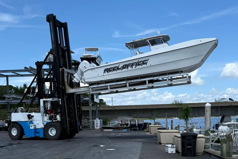 Slide: The Image of 2024 TomCat 36 boat lifted by forklift at marina, clear blue sky background. - 16