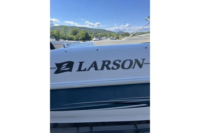 Slide: The Image of 2000 Larson SEI226 boat with logo, parked outdoors under a clear blue sky. - 1