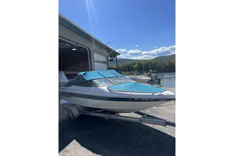 Slide: The Image of 2000 Larson SEI226 boat on trailer by lakeside, sunny day, blue cover. - 2