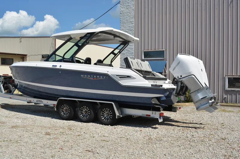 Slide: The Image of 2026 Monterey Elite 30 OB boat on trailer, parked outdoors near industrial building. - 2