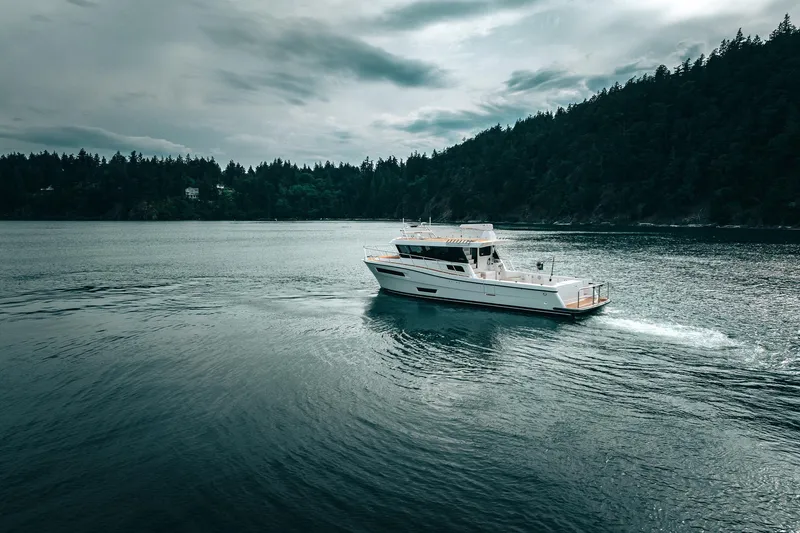 Slide: The Image of 2025 Lindell 48' yacht cruising on a serene lake with forested shoreline. - 52