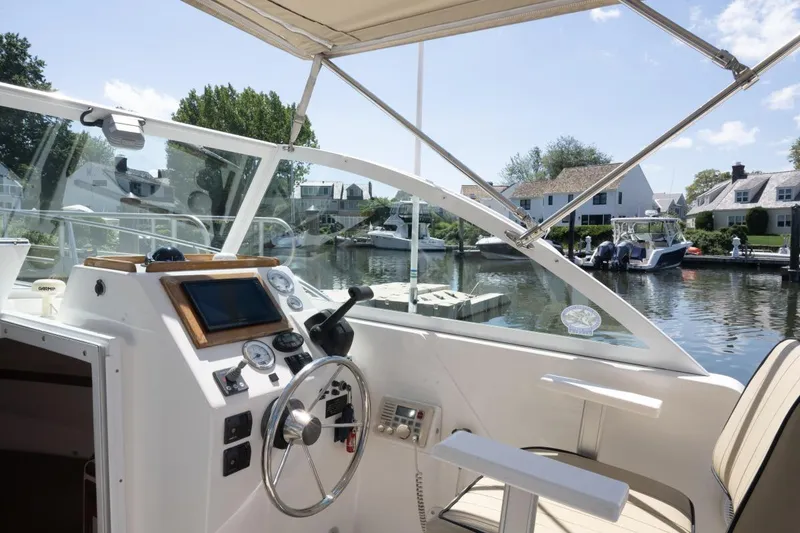 Slide: The Image of 2004 Hunt Yachts Surfhunter 25 cockpit with steering wheel, docked near waterfront homes. - 16
