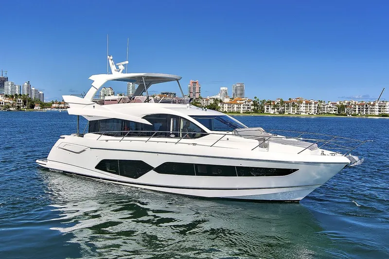 The Image of 2019 Sunseeker Manhattan 66 yacht cruising on a sunny day near coastal cityscape. - 0