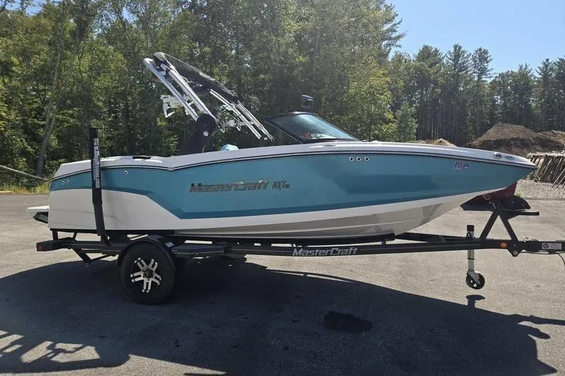 Slide: The Image of 2020 MasterCraft NXT20 boat on trailer, parked outdoors with trees in background. - 16