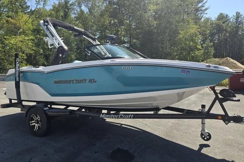 Slide: The Image of 2020 MasterCraft NXT20 boat on trailer, parked outdoors with trees in background. - 17