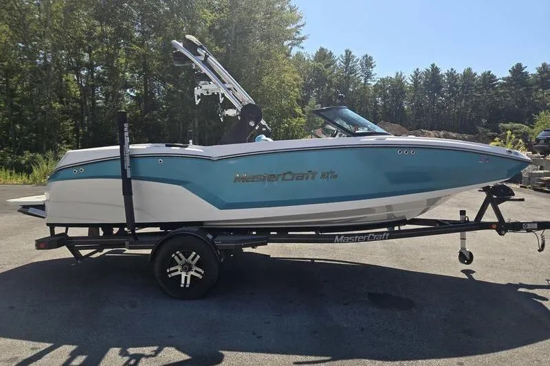 Slide: The Image of 2020 MasterCraft NXT20 boat on trailer, parked outdoors with trees in background. - 19