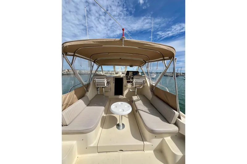Slide: The Image of 2005 Mainship Pilot 30-II boat interior with seating and table, under a canopy, docked at marina. - 14