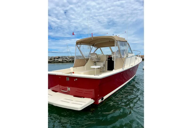 Slide: The Image of 2005 Mainship Pilot 30-II boat with red hull and beige canopy, docked in calm waters. - 2