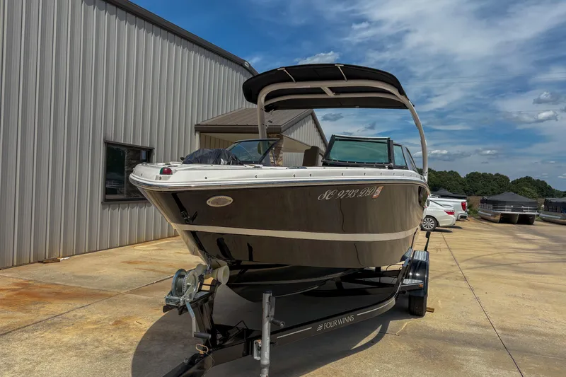 Slide: The Image of 2016 Four Winns H210 boat on trailer, parked outside a metal building under a blue sky. - 4