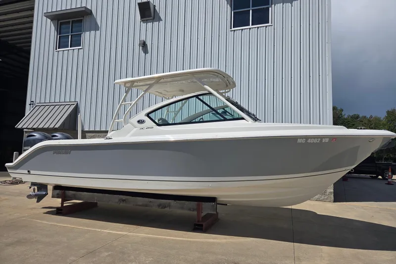 Slide: The Image of 2023 Pursuit DC 266 Dual Console boat displayed outdoors near a metal building. - 0