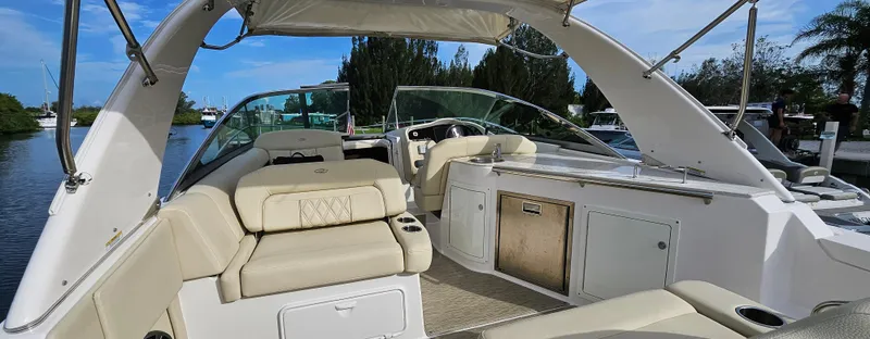 Slide: The Image of 2018 Regal 33 XO boat interior with beige seating and kitchenette, docked by a scenic waterway. - 2