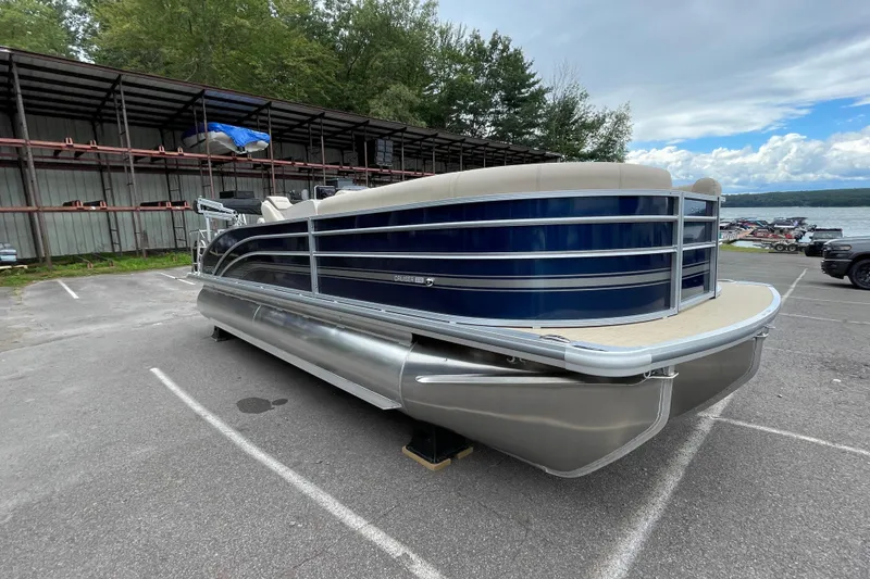 Slide: The Image of 2026 Harris Cruiser 230 pontoon boat parked near a lake under a cloudy sky. - 10