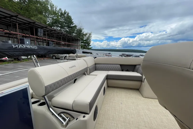 Slide: The Image of 2026 Harris Cruiser 230 pontoon boat interior with beige seating, docked by a scenic lake. - 13