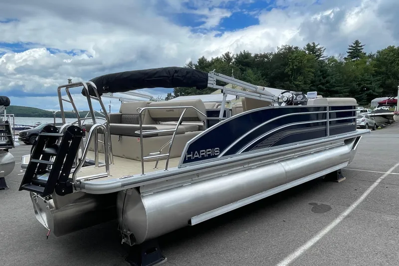 Slide: The Image of 2026 Harris Cruiser 230 pontoon boat parked on a lakeside lot under a cloudy sky. - 3