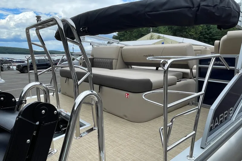 Slide: The Image of 2026 Harris Cruiser 230 boat with sleek seating and chrome railings, docked by a scenic lake. - 4