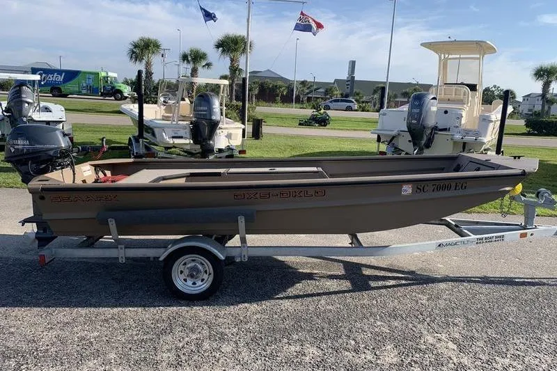 Slide: The Image of 2025 SeaArk DXS 1548 DKLD boat on trailer, parked outdoors with palm trees in background. - 4