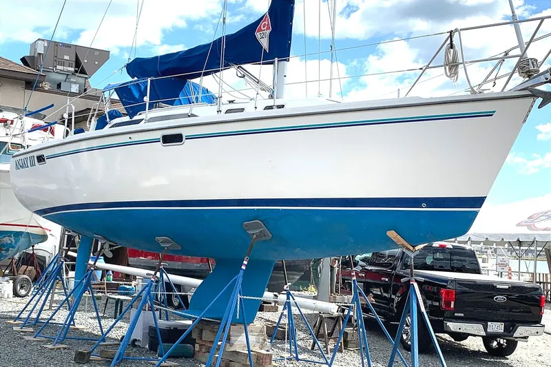 Slide: The Image of 1998 Catalina 320 sailboat on stands, blue and white hull, marina background. - 2