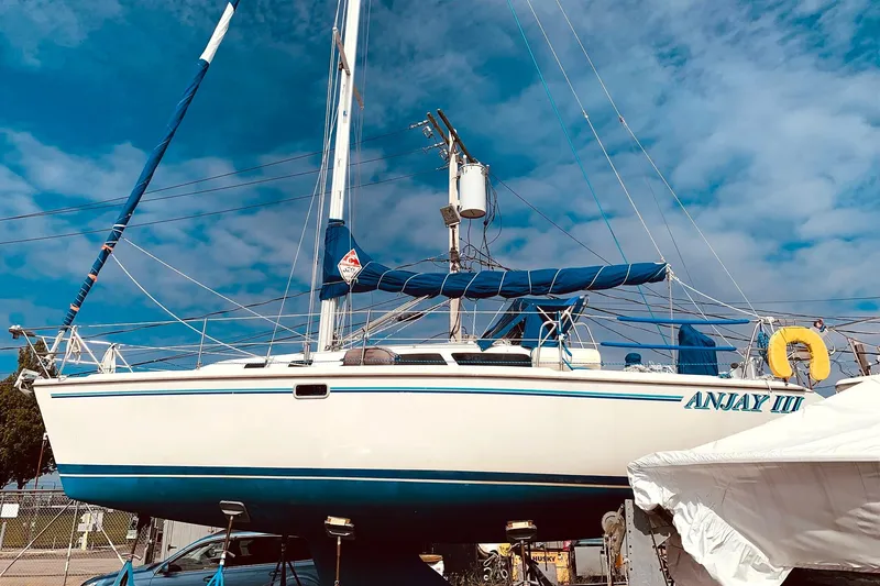 Slide: The Image of 1998 Catalina 320 sailboat on land, named "ANJAY III," under a clear blue sky. - 25