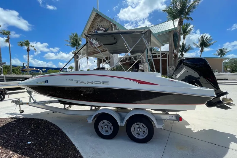 Slide: The Image of 2024 Tahoe 2150 OB boat on trailer, parked near palm trees under a clear blue sky. - 4