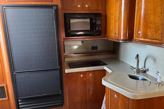 Slide: The Image of 2004 Cruisers Yachts 370 Express kitchen with wood cabinetry, sink, stove, microwave, and refrigerator. - 2