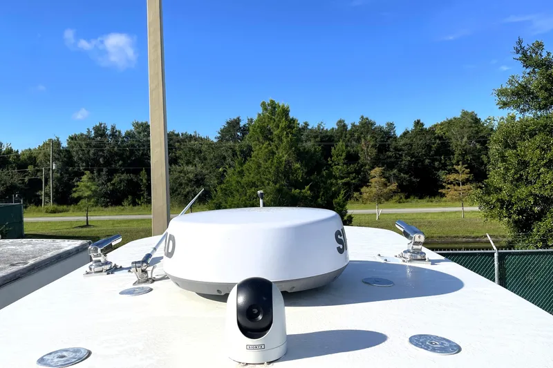 Slide: The Image of 2020 NauticStar 28 XS boat deck with radar and camera, surrounded by trees and blue sky. - 18