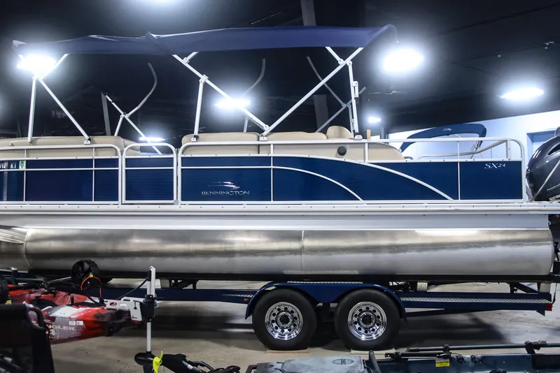 Slide: The Image of 2015 Bennington 24 SSLX pontoon boat with blue and white design on trailer indoors. - 3