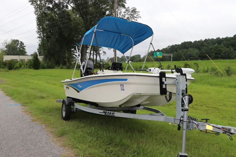 Slide: The Image of 2023 Mako Pro Skiff 13 CC boat on trailer with blue canopy in grassy area. - 2