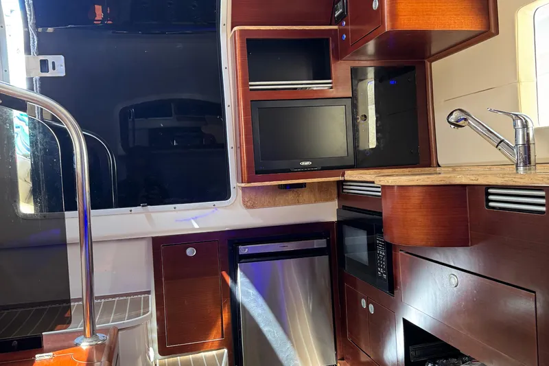 Slide: The Image of Interior of a 2016 Edgewater 370CC boat featuring a kitchenette with wood cabinetry and appliances. - 43