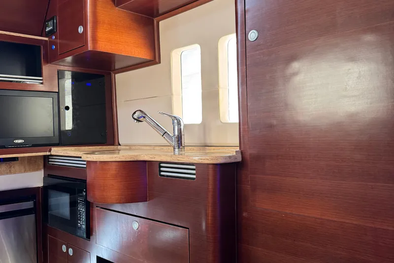 Slide: The Image of Interior of 2016 Edgewater 370CC boat featuring a modern kitchenette with wood finish. - 44